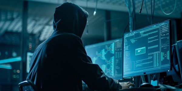 Hooded hacker working on multiple computers.